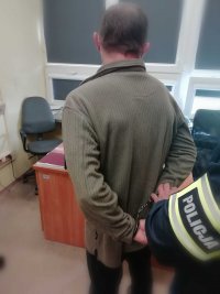 biuro w budynku komendy, policjant zakłada kajdanki zatrzymanemu mężczyźnie