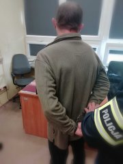 biuro w budynku komendy, policjant zakłada kajdanki zatrzymanemu mężczyźnie