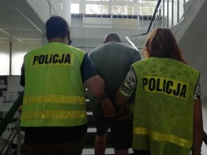 Mężczyzna i dwóch policjantów w kamizelkach z napisem Policja wchodzący po schodach