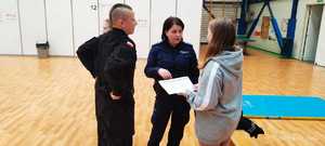 Policjantka, uczeń klasy policyjnej rozmawiają z kobietą na hali sportowej