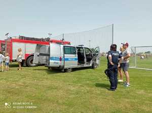 Radiowóz i wóz strażacki na stadionie, uczestnicy imprezy plenerowej i policjantka