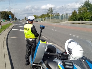 policjant uchu drogowego obserwuje ruch na drodze obok stoi policyjny motocykl