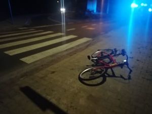 Rower leżący przy przejściu dla pieszych, w tle światła policyjne.