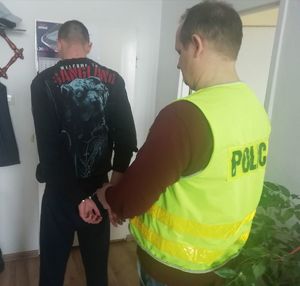 Policjant zakłada mężczyźnie kajdanki w pokoju służbowym.