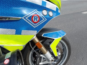 przednia część policyjnego motocykla na drodze. niebieskie i żółte elementy lakieru i okleiny motocykla, na motocyklu w czerwonym rombie znak R, ruchu dogowego.  po prawej stronie koło motocykla.