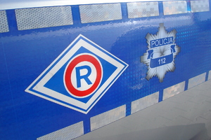 na drzwiach radiowozu na niebieskim tle znajdują się: logo gwiazda policyjna oraz znaczek ruchu drogowego - litera r umieszczona w czerwonym kółku i dalej w  rombie.