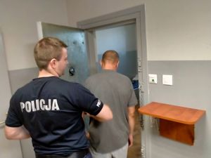 Policjant wprowadza mężczyznę do pokoju zatrzymań