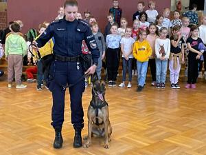 Policjantka i pies służbowy na hali sportowej, w tle dzieci