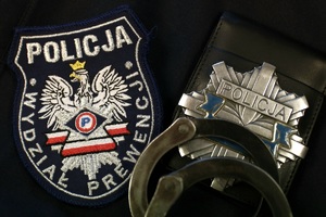 Naszywka Wydziału Prewencji, obok policyjna odznaka oraz kajdanki.