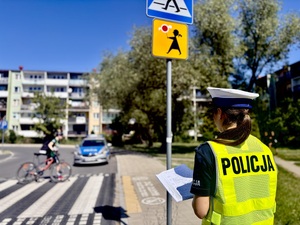 Umundurowana policjanta stojąca przy przejściu dla pieszych znajdującym się przy szkole.