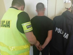 pomieszczenie w komendzie, nieumundurowany policjant w kamizelce odblaskowej wyprowadza zatrzymanego mężczyznę