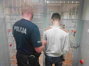 Policjant i mężczyzna na tle krat w areszcie policyjnym