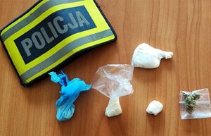 kilka kulek białej substancji w foli na biurku obok opaska z napisem policja