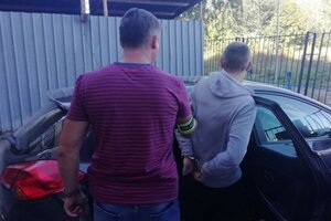 Dwóch policjantów i mężczyzna z kajdankami na rękach przy samochodzie