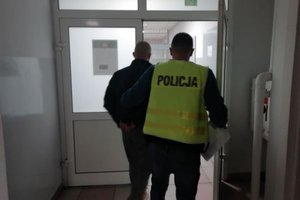 Mężczyzna z kajdanki na rękach z tyłu i policjant w drzwiach