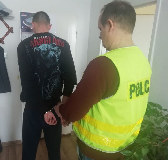 Policjant zakłada mężczyźnie kajdanki w pokoju służbowym