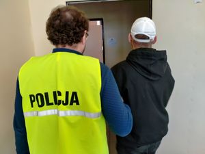 Policjant w kamizelce i mężczyzna przechodzą przez drzwi