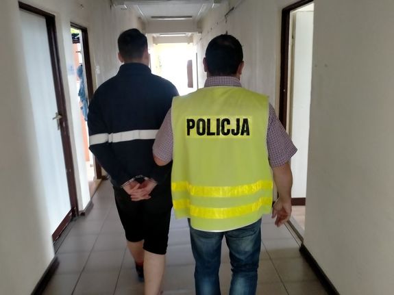 Mężczyzna z kajdankami z tyłu, obok policjant