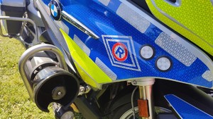 fragment motocykla policyjnego, a na nim znak ruchu drogowego w kształcie rombu.