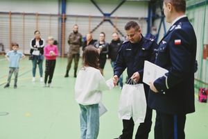 Policjant wręcza nagrodę dziecku na hali sportowej.