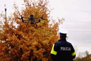 Policjant stojący tyłem i w tle dron policyjny.