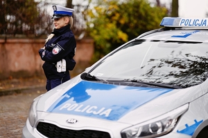 Umundurowany policjant z Wydziału Ruchu Drogowego obok radiowozu.