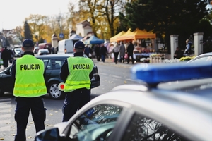 Dwóch policjantów stojących przy cmentarzu nadzorujący płynność ruchu drogowego.