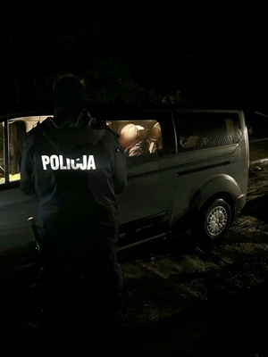 Policjant z zatrzymanymi cudzoziemcami znajdującymi się w aucie Straży Granicznej.
