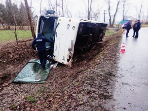 Policjant przy autobusie przewróconym na prawy bok znajdującym się w przydrożnym rowie.