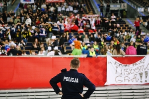 Policjant stojący tyłem a w tle kibicująca młodzież.