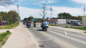 Kolumna pojazdów prowadzona przez policjanta na motorze policyjnym.