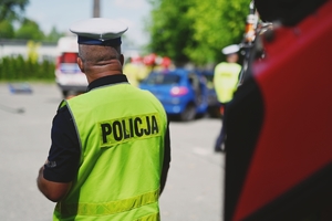 Policjant ruchu drogowego stojący tyłem w kamizelce odblaskowej.