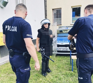 Policjanci pomagający ubrać się nastolatkowi w strój policjanta.