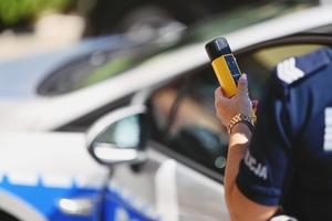 Policjantka trzymająca urządzenie do pomiaru trzeźwości na tle radiowozu.