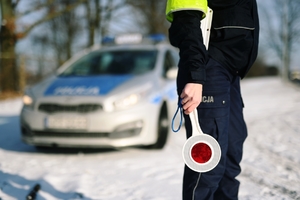 Tarcza policyjna trzymana przez policjantkę, w tle radiowóz.