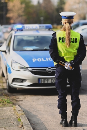 Policjantka stojąca tyłem na tle radiowozu.