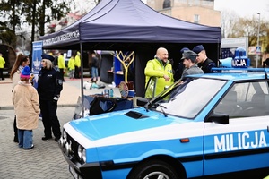 Policyjne stanowisko, radiowozy oraz funkcjonariusze przeprowadzający rozmowy z mieszkańcami.