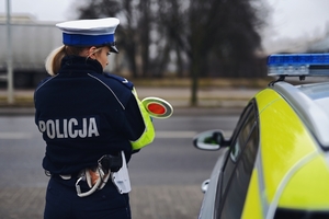 Policjantka ruchu drogowego z tarczą, stojąca przy radiowozie.