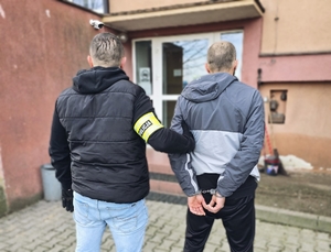 Kryminalny doprowadzający do komendy zatrzymanego mężczyznę.