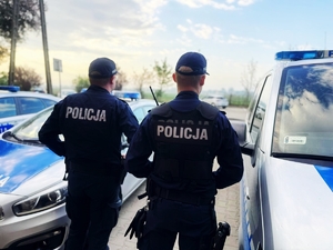Policjanci stojący obok radiowozów.