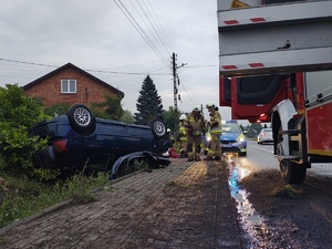 Auto, które leży w rowie, obok pracujące na miejscu służby ratunkowe.