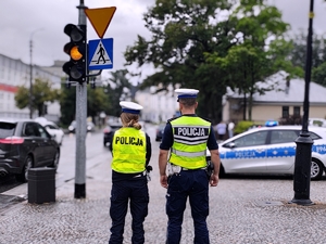 Policjanci przy radiowozie stojący tyłem.
