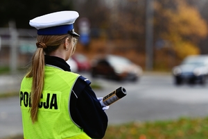 Policjantka stojąca tyłem trzymająca urządzenie do badania kierowców na zawartość alkoholu w organizmie.