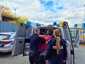 Policjanci z zatrzymanym przy radiowozie.