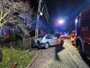 Miejsce zdarzenia drogowego, wozy strażackie, uszkodzony pojazd przy słupie energetycznym.