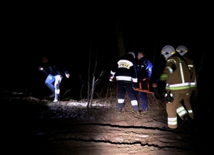 Transport mężczyzny przez las, jeden z policjantów oświetla drogę.