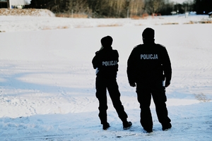 Policjanci obserwujący zamarznięty akwen w śnieżnej aurze.