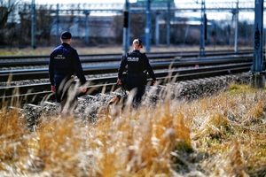 Policjant wraz z Strażą Ochrony Kolei podczas kontroli, w tle tory kolejowe.