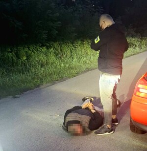 Nieumundurowany policjant stoi przy zatrzymanym mężczyźnie.