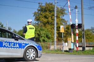 Policjant a w tle przejazd kolejowy.